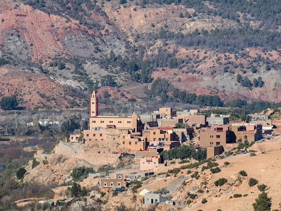 Wide valley panorama with stone village and orchards framed by rugged mountains.