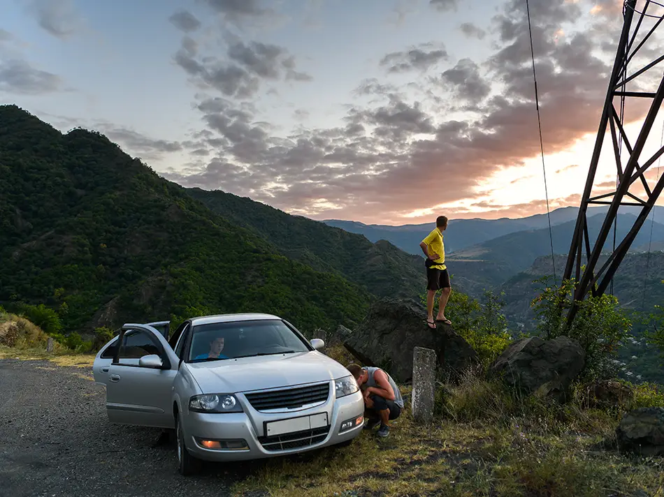 Traveler stands by roadside tower at sunset overlooking deep green mountains.