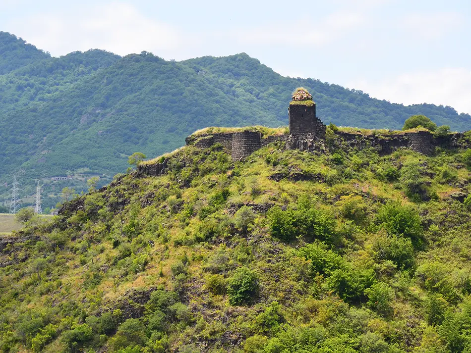A lone watchtower stands on a green ridge beneath distant hills and sky.