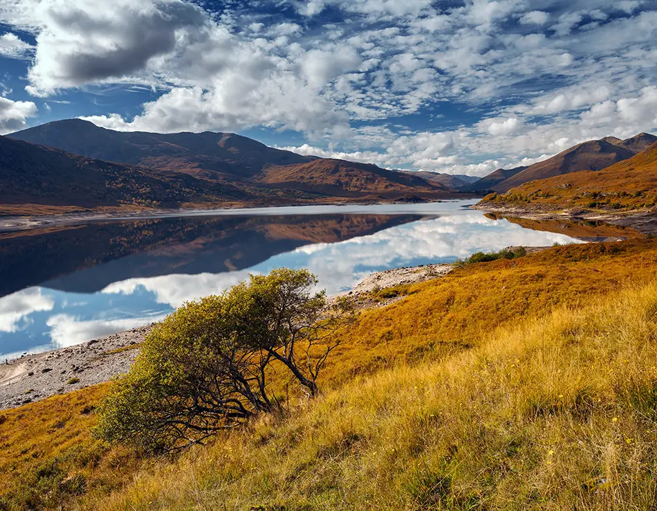 Loch reflecting rugged mountains and russet moorland under a dramatic evening sky.