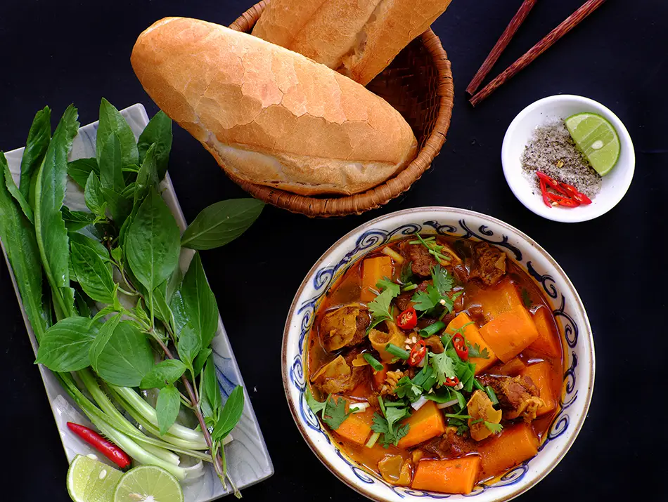 Rich bò kho beef stew with carrots and fresh herbs, a typical Vietnamese food to enjoy with bread.