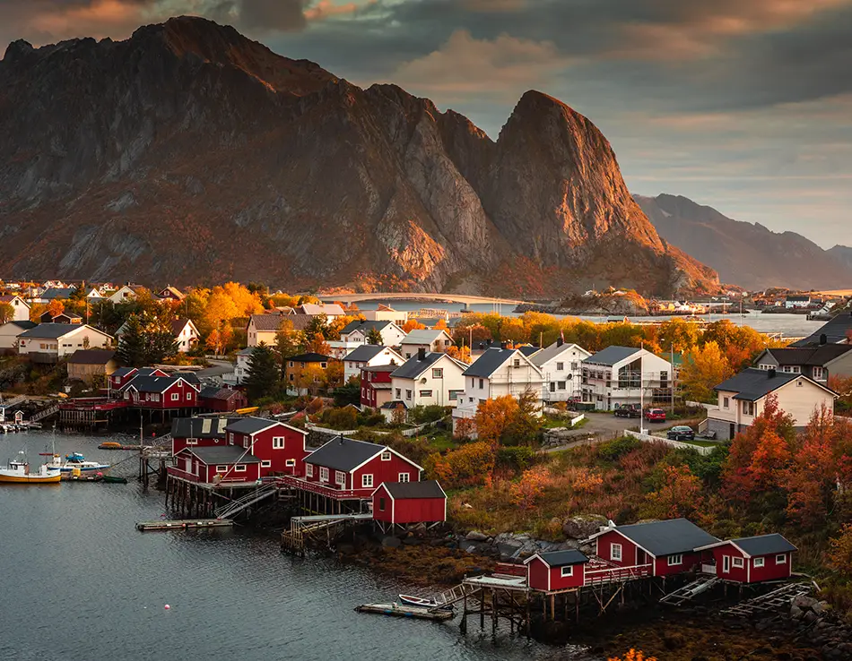 Harbor cabins and fishing boats beneath jagged peaks tinted with late-season color.