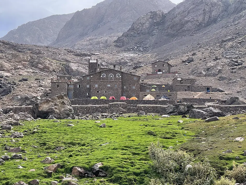 Mountain refuges cluster in a barren valley beneath layered ridgelines.