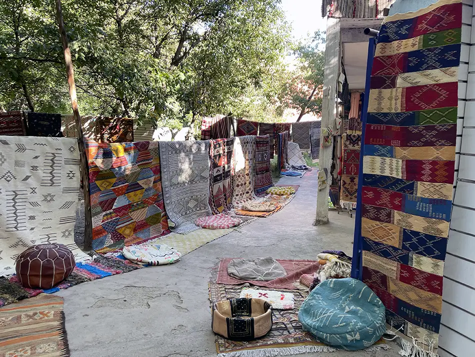 Colorful carpets hang in a shady lane, showcasing Imlil in Morocco.