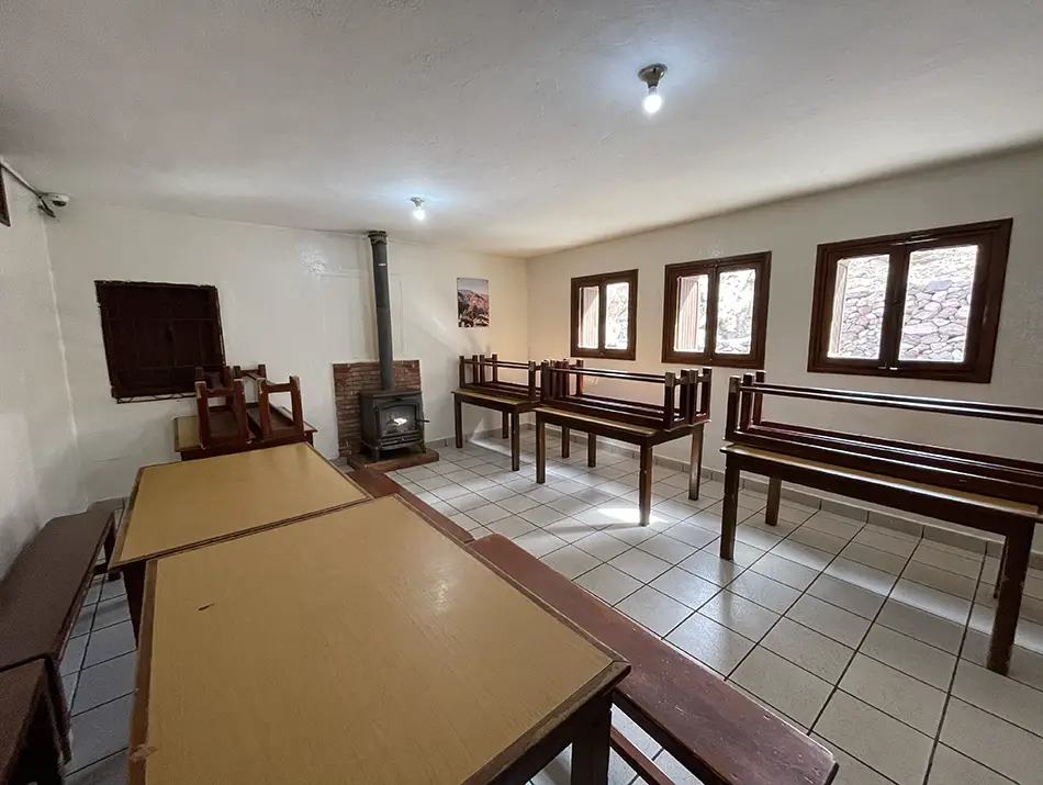 Simple dining hall inside the mountain refuge with wooden tables and bunks.