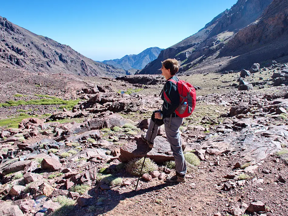 Hiker with red backpack on rocky trail in the High Atlas.