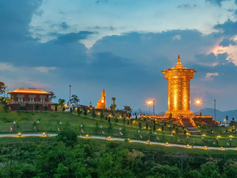 Golden prayer wheel and hillside temple illuminated at dusk at Samten Hills