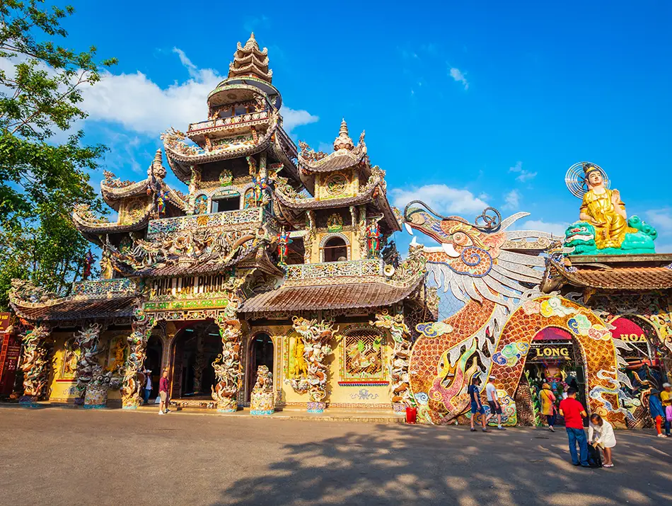 Colorful mosaic-covered Linh Phuoc Pagoda in Dalat with dragon sculptures, ornate towers, and a golden Buddha statue above the gate, one of the top attractions in Dalat.