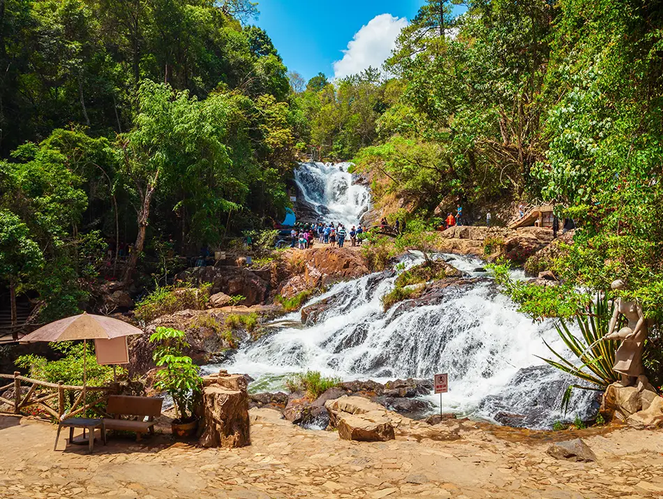 Visitors admire cascading white water amid lush forest at Datanla Waterfall.