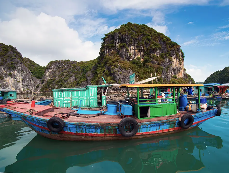 Old wooden boat floating near limestone cliffs, capturing the debate on whether Cat Ba is worth visiting.