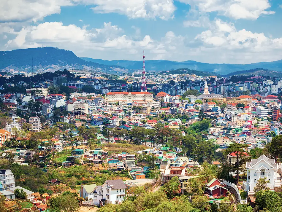 Aerial cityscape with colorful rooftops surrounded by rolling green hills and cool highland air.