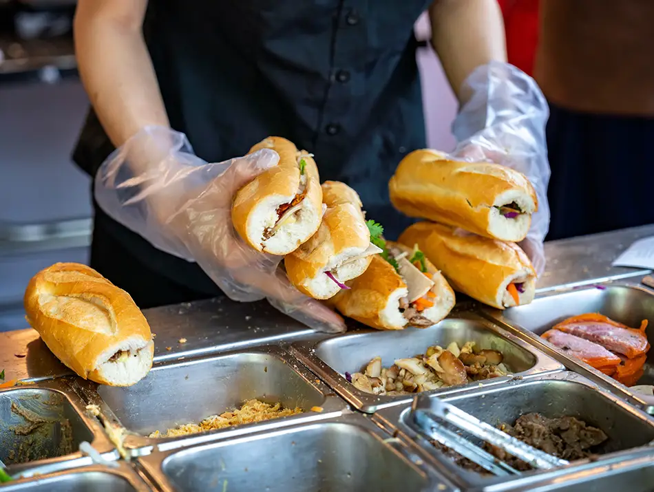 Woman preparing banh mi sandwich at a street stall.