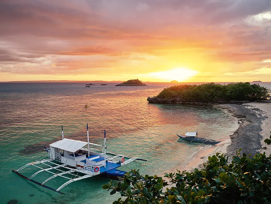 Traditional outrigger boats resting by the shore at sunset on Malapascua island