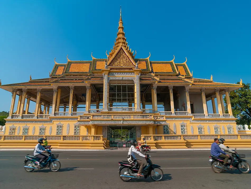 Elegant Royal Palace facade with motorbikes passing by, one of the best places to visit in Cambodia.