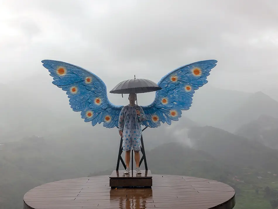 A butterfly-winged viewpoint statue rises above misty mountain slopes on a foggy Sapa morning.