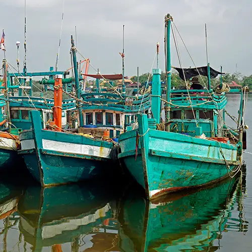 Turquoise fishing boats are moored side by side along the Kampot harbor.
