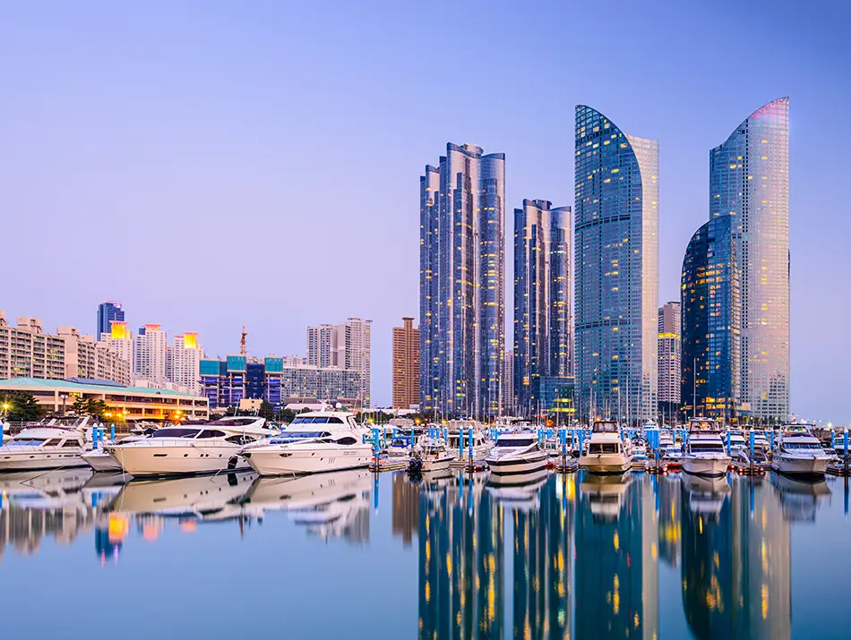 Tall waterfront skyscrapers and marina reflections in Busan at dusk.