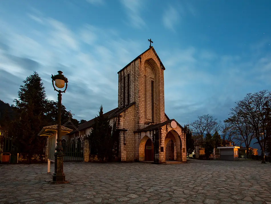 Sapa Stone Church stands illuminated at dusk beside the quiet, open town square.