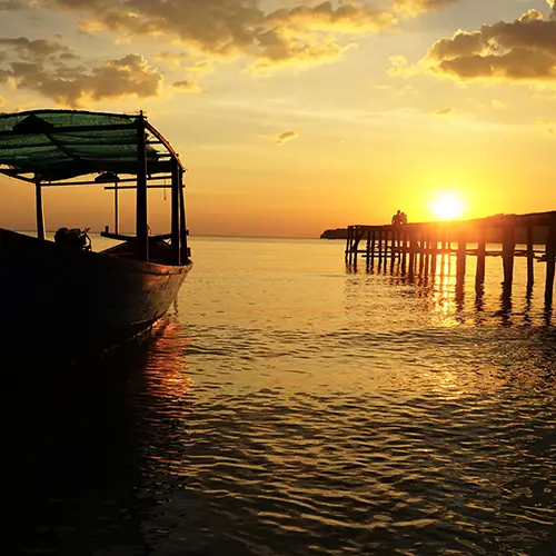 Boat floating by a pier at sunset