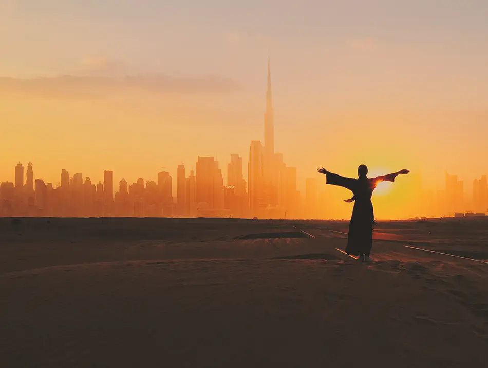 A traveler stands facing the skyline at sunset