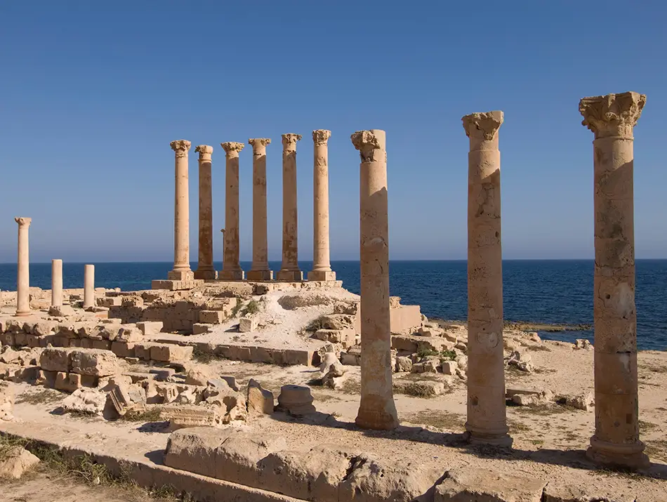 Ancient Roman columns overlooking the Mediterranean coast in calm light.