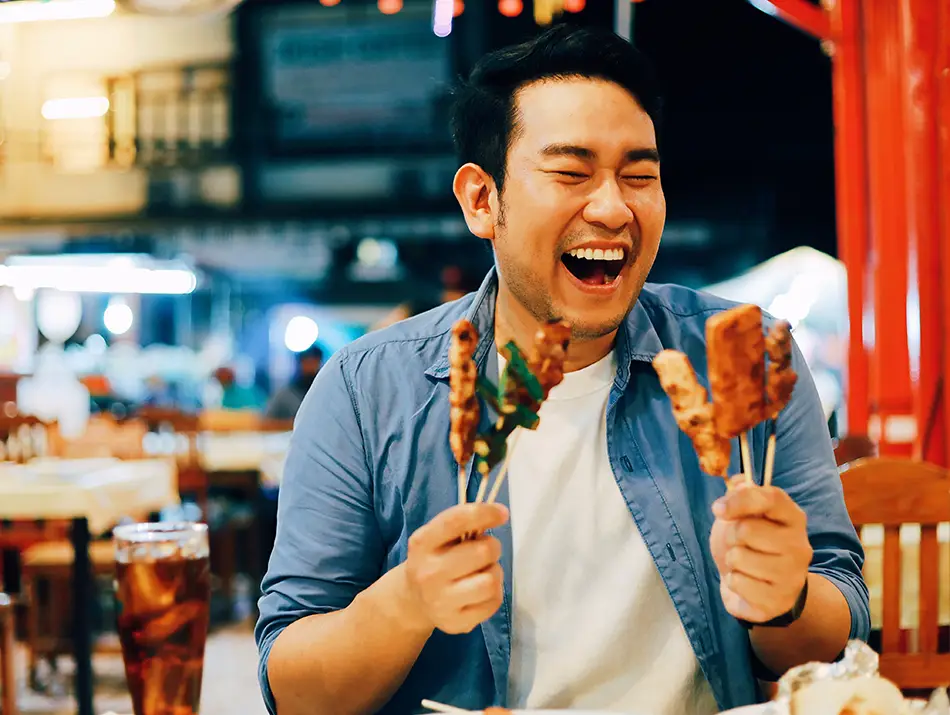 Traveler enjoying grilled skewers at a lively night market in a best foodie country.