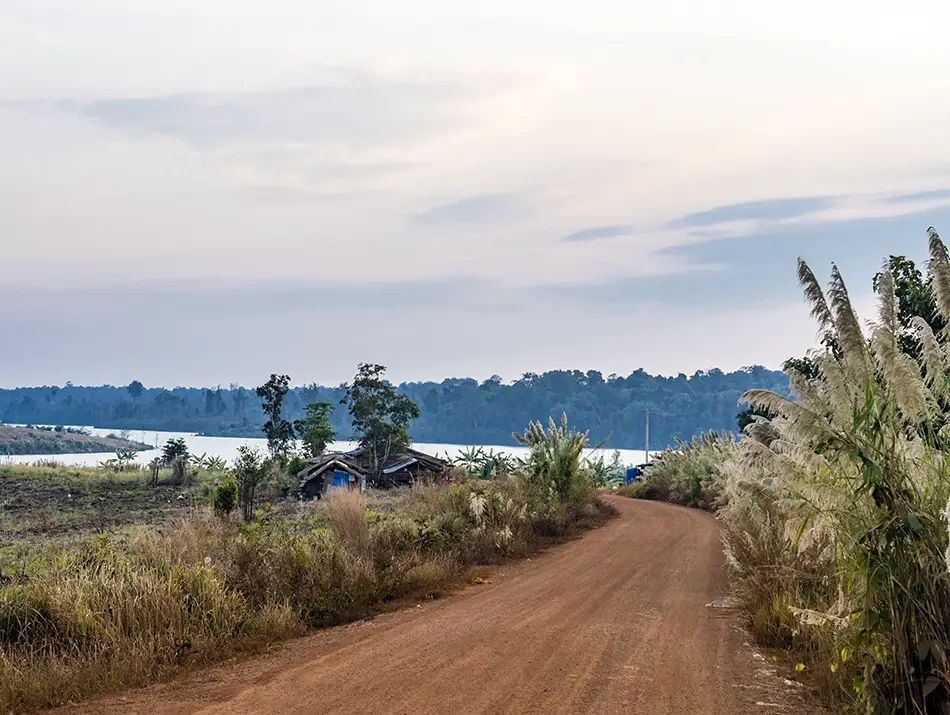 Dirt road curving along the lake near Atai Dam, surrounded by grassy hills.