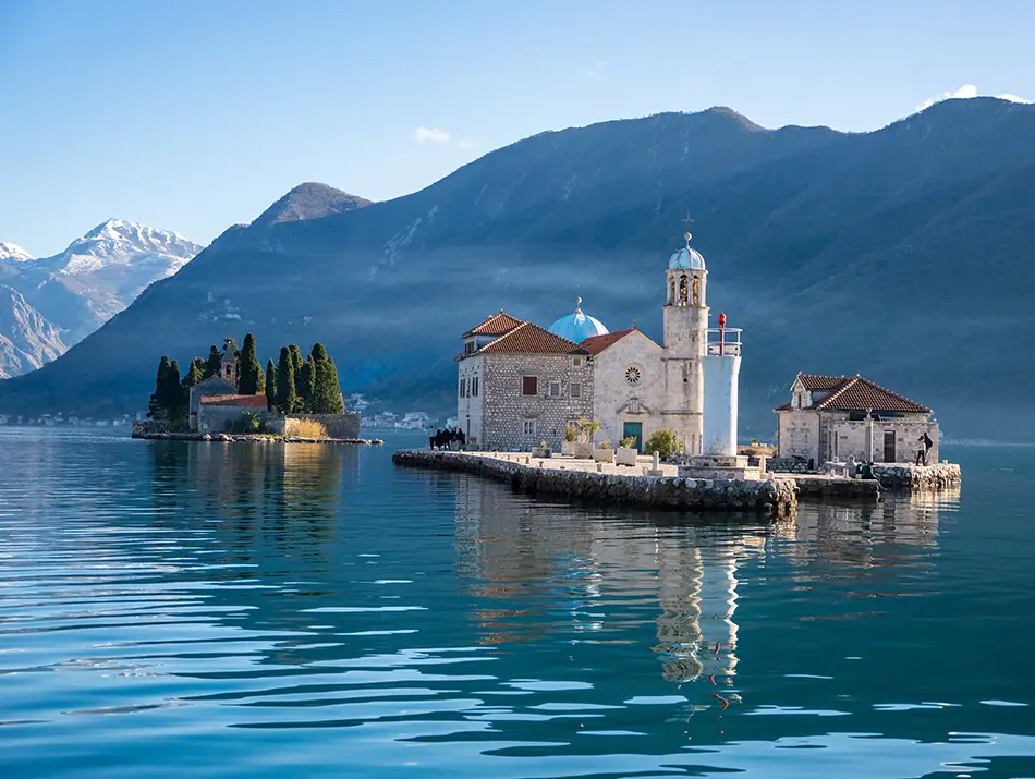 Small stone church sitting on a quiet islet surrounded by calm waters and rising mountains.