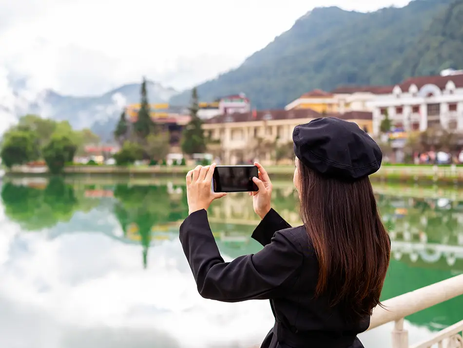A traveler photographs Sapa’s calm lakeside and mountain backdrop