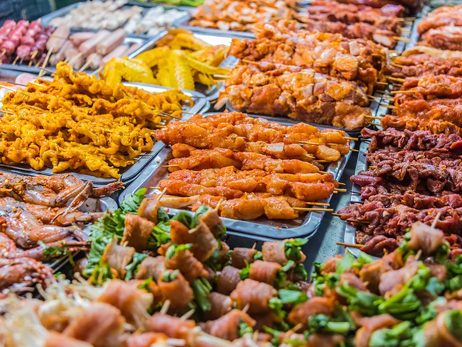 A colorful street stall shows assorted grilled meats and skewers arranged across a busy Sapa market table.