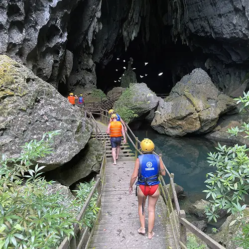 Visitors walk through shallow water toward the narrow entrance of Dark Cave.
