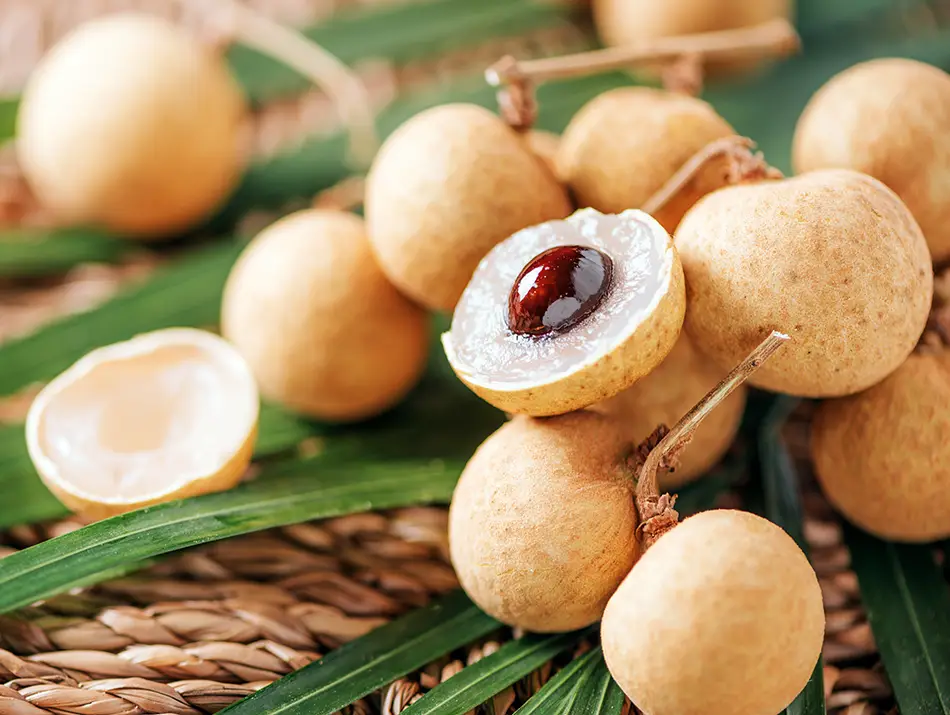 Longan fruits with one peeled open to show its translucent flesh and dark seed, a common favorite among Vietnamese fruits.