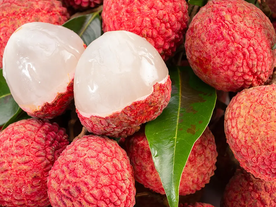 Fresh lychees with rough red skin, two peeled open to reveal their glossy, translucent white flesh.