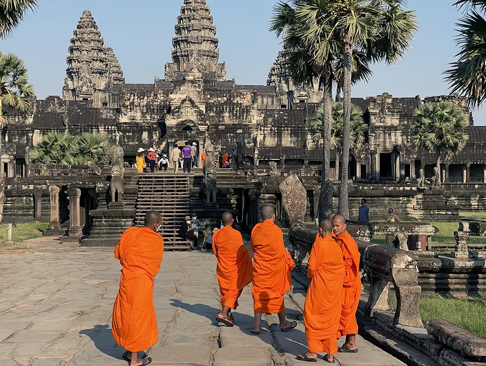 Monks in saffron robes walk toward Angkor Wat, one of the best tourist places in Cambodia.
