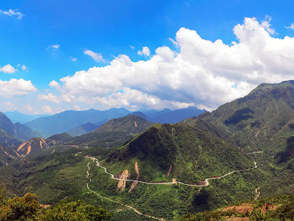 A sweeping view of O Quy Ho Pass reveals winding mountain roads cutting through deep green valleys.