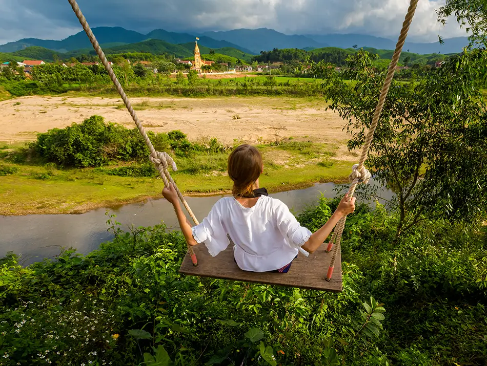 A traveler on a riverside swing enjoys views answering if Phong Nha is worth a visit
