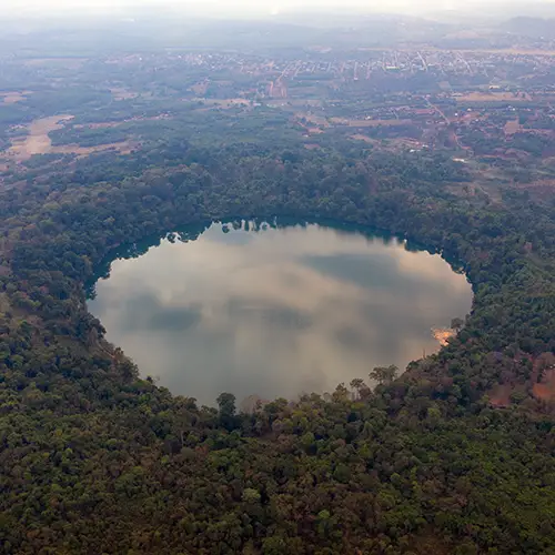 Aerial shot of round volcanic lake encircled by dense forest, a hidden gem in Cambodia.