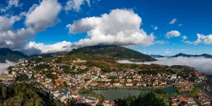 A wide panoramic view of Sapa town surrounded by bright clouds and terraced hills.
