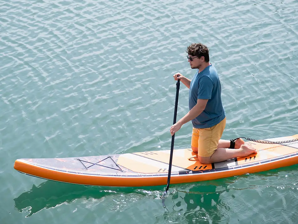 A man kneels on a paddleboard gliding across calm water, enjoying one of the best things to do in Phong Nha.