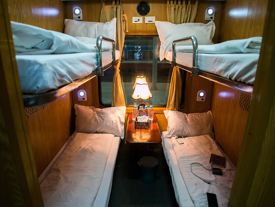 Warm wooden bunks and soft lighting inside an overnight sleeper cabin illustrate a comfortable way for how to get to Sapa.