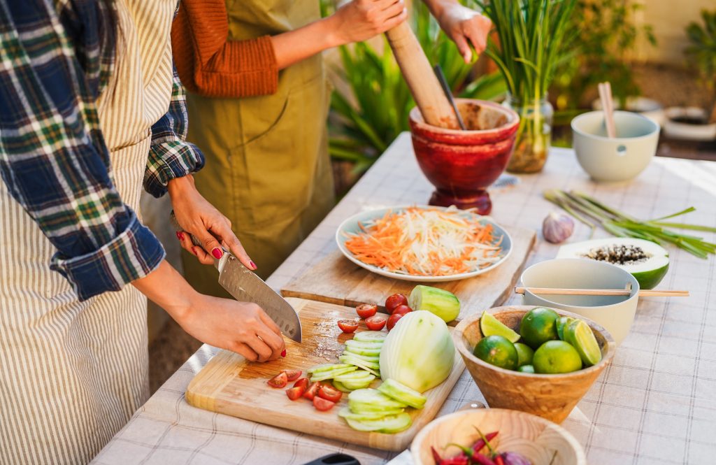 Hands prepare fresh vegetables and herbs during a lively outdoor Vietnamese cooking class.