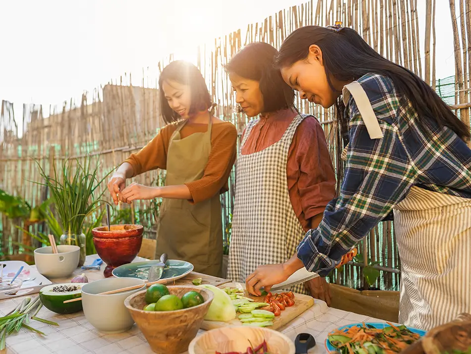 Three Vietnamese women preparing vegetarian dishes together at an outdoor cooking table.