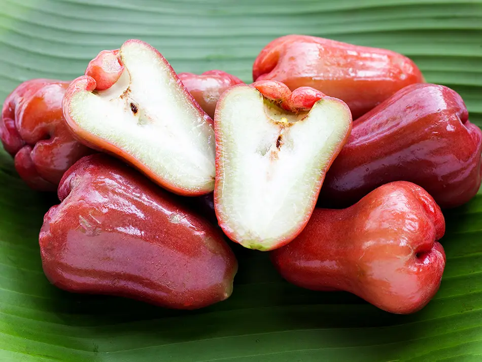 Fresh rose apples arranged on a banana leaf, with one fruit cut open to show its crisp, pale interior.