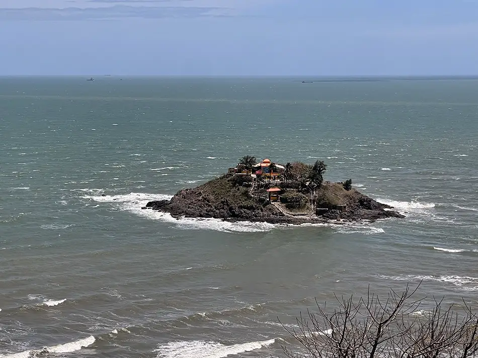
Small rocky island topped with a temple rising from the calm sea.