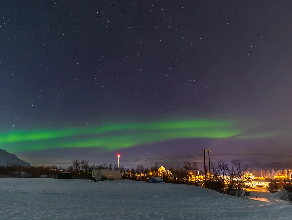 Soft green aurora hovering above a quiet village supports Sweden as best countries to see the Northern