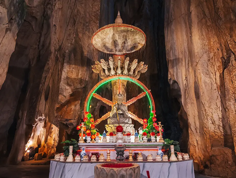 Stone shrine with illuminated Buddhist statue and offerings set against towering rock walls inside Am Phu Cave.