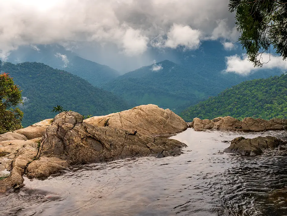 Natural rock pools overlooking misty mountains and forests in the distance.