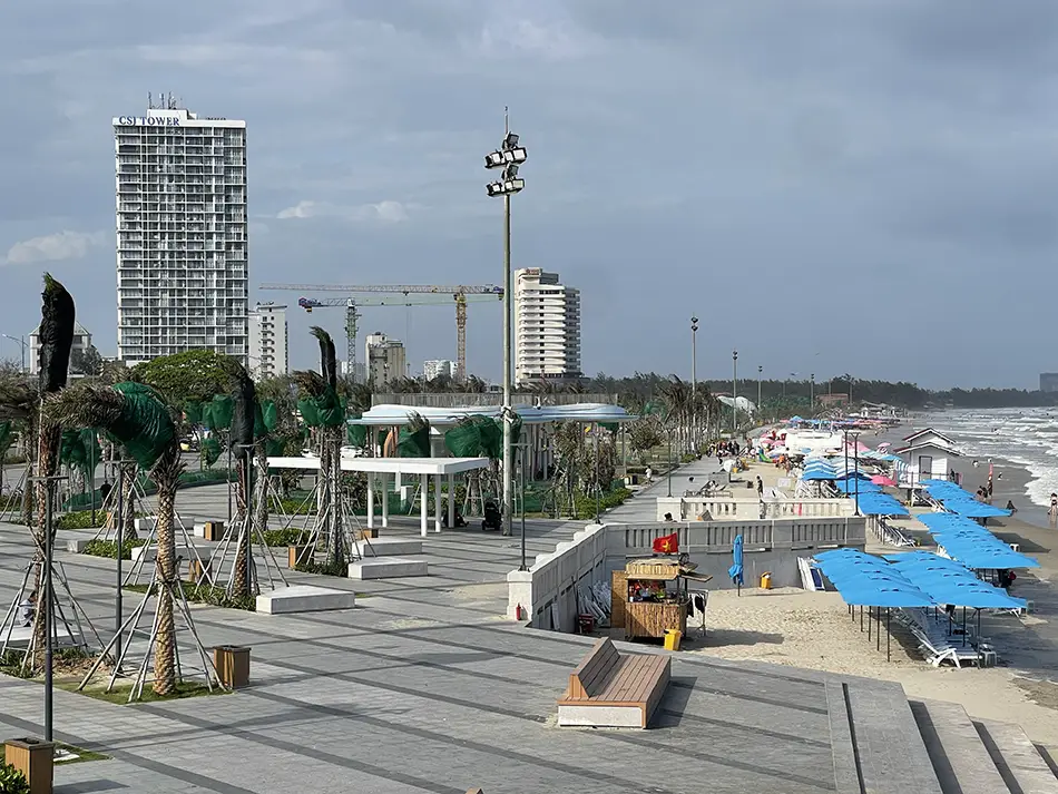 Beachfront construction site with cranes and high-rise buildings under a cloudy sky.