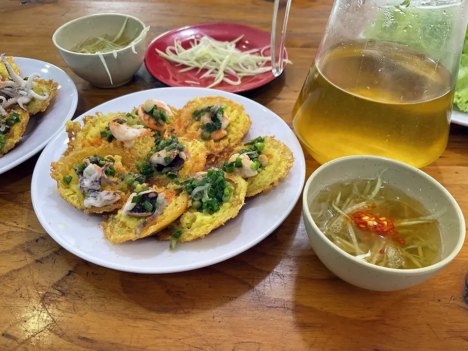 
Plates of crispy banh khot mini pancakes served with fresh herbs and dipping sauce.