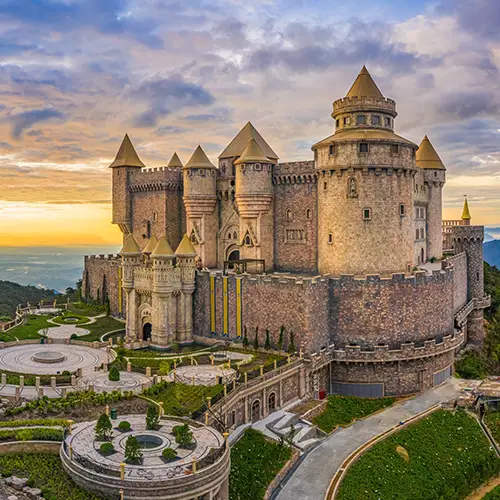 A large stone castle complex overlooking the gardens and surrounding peaks.
